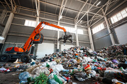 Grabbing excavator collects garbage in plant warehouse