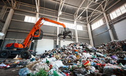 Grabbing excavator collects garbage in plant warehouse